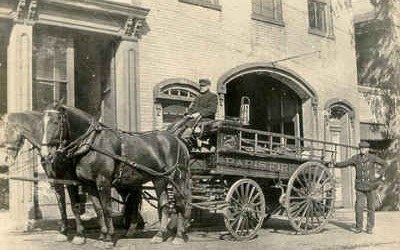 Historic black-and-white photo of a horse-drawn Paris fire engine outside the fire station.