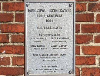 Metal plaque on a brick wall reading Municipal Incinerator, Paris, Kentucky, 1966, listing the mayor, commissioners, engineers and contractors.