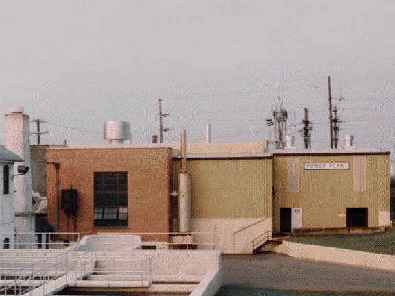 Tan brick building with a Power Plant sign, with treatment basins in the foreground.