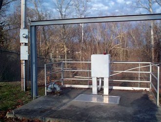Fenced concrete equipment pad with a control panel.