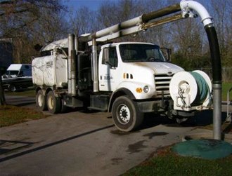 Utility truck with a large vacuum hose boom raised.