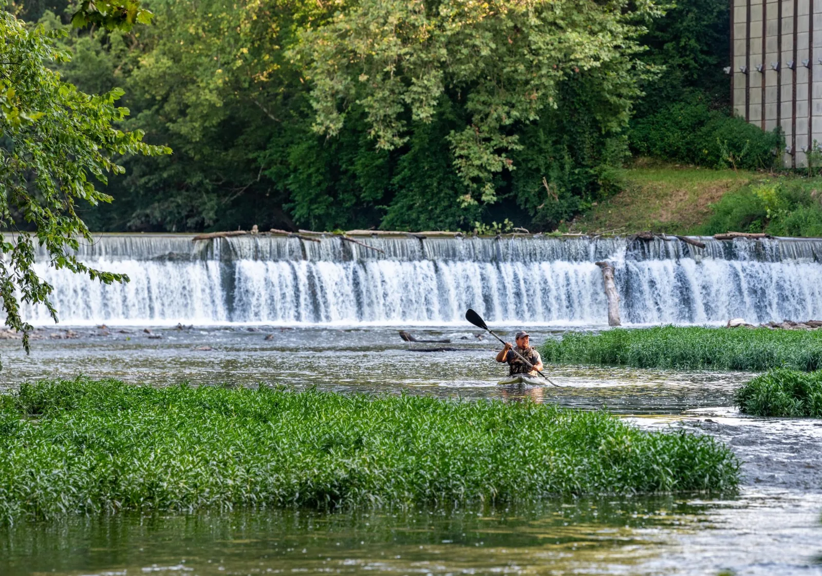 Kayaker paddling below a low dam on a creek