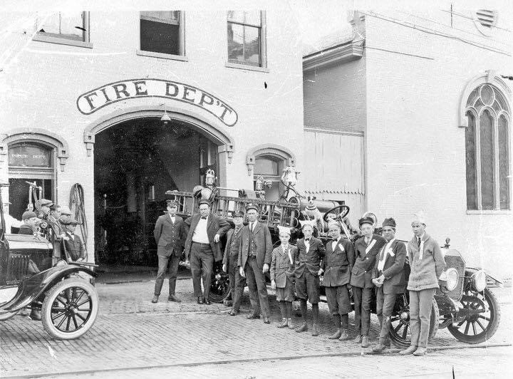 Historic black-and-white photo of Paris firefighters standing with early fire vehicles in front of a station marked Fire Dept.