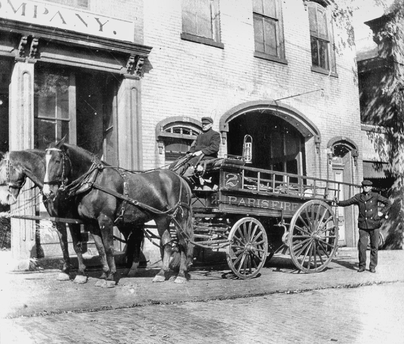 Historic black-and-white photo of a horse-drawn Paris fire engine outside the fire station.