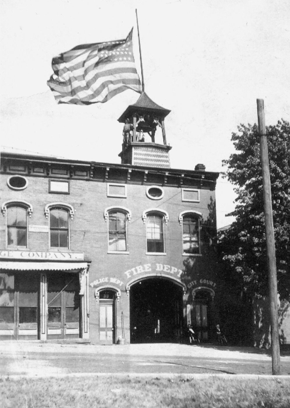 Historic black-and-white photo of the brick building that housed the Paris fire and police departments and city court, with a bell tower and flag.